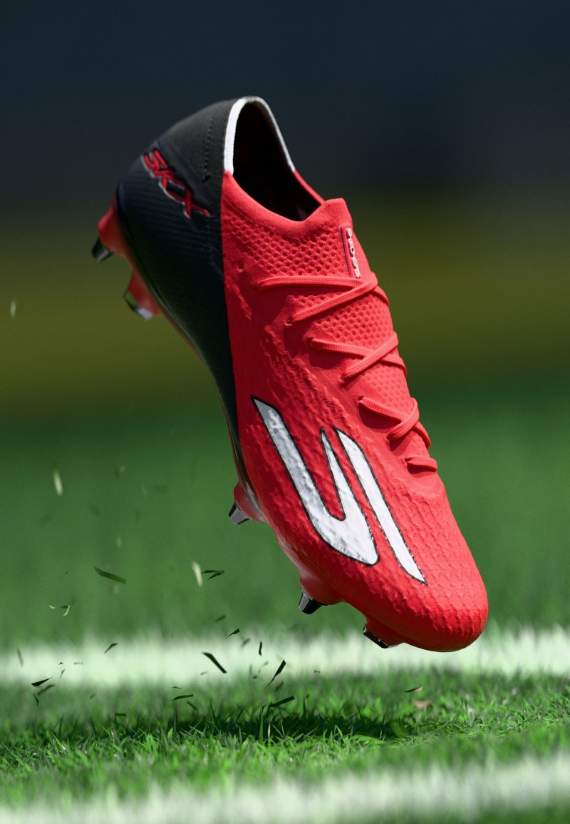 Botín de fútbol rojo y negro con logo blanco, en el aire sobre un campo de césped con césped levantado y línea de límite blanca visible.