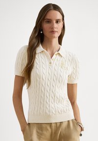 Cable-stickad pikétröja i krämfärg, med krage, korta ärmar och ribbad nederkant. Har broderad logotypdetalj i guld.