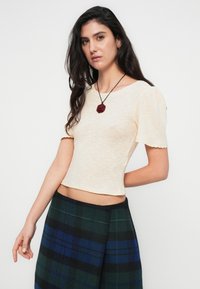 Κοντομάνικο πάνω μέρος σε κρεμ απόχρωση με ραβδώσεις και στρογγυλή λαιμόκοψη, σε συνδυασμό με φούστα καρό σε σκούρο πράσινο και μπλε. Υφή υφάσματος, εφαρμοστή γραμμή.