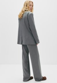 Sacou gri, ajustat, cu o deschidere simplă, asortat cu pantaloni gri cu pantaloni largi. Modelul poartă pantofi maro slip-on, evidențiind o potrivire relaxată.
