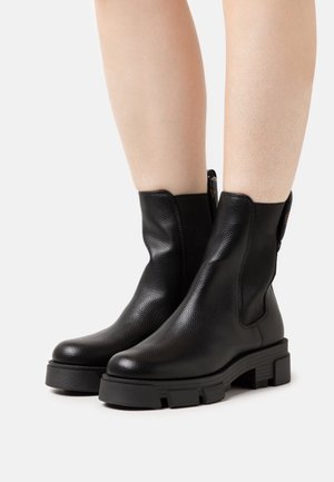 Mustat nahkaiset nilkkurit, joissa on teksturoitu pinta, joustavat sivupaneelit ja paksu kumipohja. Vahvistettu korko ja minimaliset metalliosat.