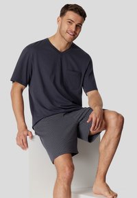 Navy V-Ausschnitt T-Shirt mit einer Brusttasche, kombiniert mit gemusterten grauen Shorts. Die Shorts haben kleine weiße Punkte auf einem dunklen Hintergrund.