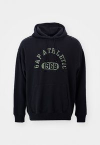 Sudadera negra de tejido suave, con bolsillo canguro, capucha con cordón y una impresión gráfica verde que dice "GAP ATHLETIC 1969."
