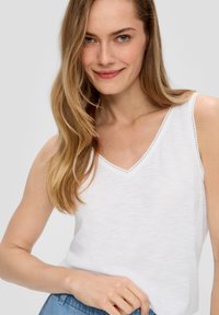 Witte mouwloze top met een V-hals en decoratieve stiksels langs de randen; lichtgewicht, zachte textuur; gecombineerd met denim.
