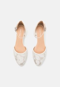 Vita spets slingback-skor med rund tå och en smal ankelrem. Slät innerfoder och blommig spetstextur på ovandelen.