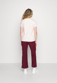 Ljusrosa bomulls-t-shirt, korta ärmar, kombinerad med vinröda kordbyxor. Vita sportskor. Bakifrån, neutral bakgrund.