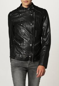 Svart läderjacka med silverdetaljer, dubbelknäppt design, stå-up krage, framfällbar dragkedja och knappstängning, samt två fickor med dragkedja.