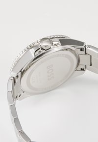 Ασημένιο ρολόι από ανοξείδωτο χάλυβα με γυαλιστερή φινίρισμα, διαθέτοντας υφασμένο bezel, χαραγμένο κορώνα και αδιάβροχη θήκη.