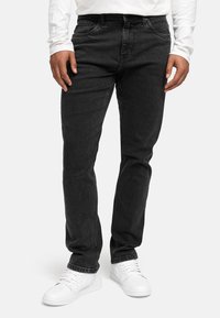 Svarte denimjeans med rett passform, fem lommer og synlig søm, kombinert med hvite sneakers og en langermet hvit skjorte.
