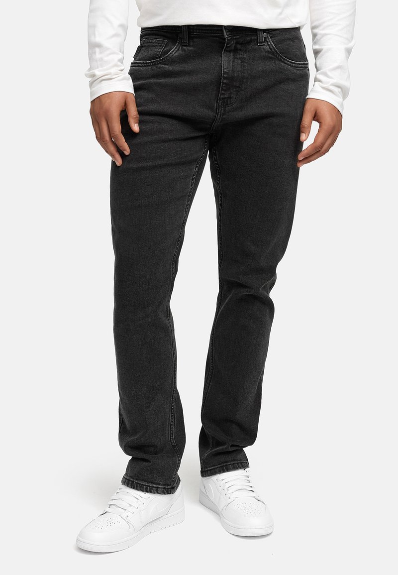 Svarte denimjeans med rett passform, fem lommer og synlig søm, kombinert med hvite sneakers og en langermet hvit skjorte.