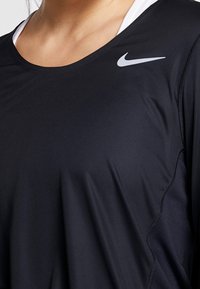 Musta urheilu toppi, joka on valmistettu sileästä ja kevyestä materiaalista. Siinä on leveä kaula-aukko, lyhyet hihat ja pieni valkoinen Nike-logo rinnassa.