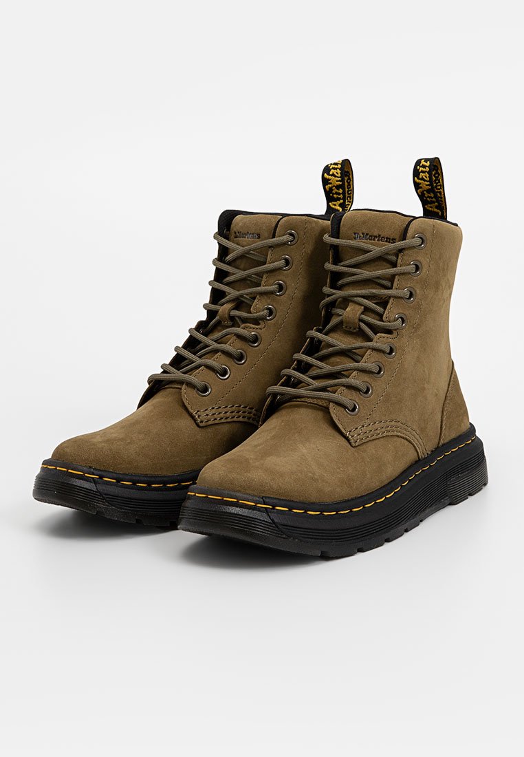 Botas de tobillo de ante marrón con suelas de goma negras, que presentan costuras amarillas, cordones redondos y una etiqueta de tirón con la marca en la parte trasera.
