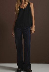 Top nero senza maniche abbinato a jeans svasati blu scuro. Il tessuto è liscio, con dettagli di cucitura discreti sulle tasche e sull'orlo.