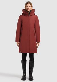 Parka imperméable rouge avec une capuche, des poches latérales zippées et une coupe droite. Elle possède une texture lisse et un ourlet ajustable.