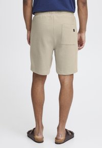Shorts texturati bej cu un talie elastică și un buzunar pe spate, asortați cu sandale maronii. Materialul prezintă un model discret de rețea.