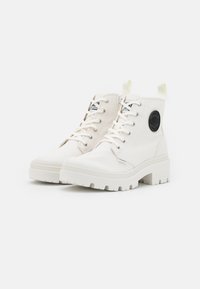 Bottines blanches en toile avec une semelle texturée, dotées d'une fermeture à lacets, d'un patch logo sur le côté et d'une bride à l'arrière du talon.