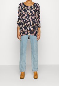 Blommig tunika med mörkblå bakgrund, trekvartsärmar, sidofrackar, tillsammans med ljusblå raka jeans och tanfärgade ankelskor.