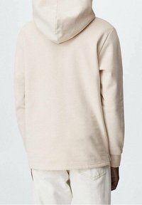 Felpa beige con una texture morbida, tasca a marsupio e cappuccio con coulisse. L'orlo è leggermente più lungo sul retro, pensato per il comfort.