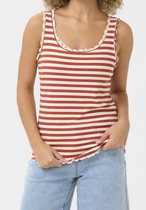 Kobieta nosząca bezrękawnik prążkowany w czerwono-białe poziome paski z falbankowymi brzegami, w połączeniu z jasnoniebieskimi jeansami.