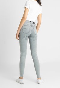 Vaqueros ajustados de un gris claro, fabricados en denim, con una cintura de altura media, cinco bolsillos y un ajuste ceñido, combinados con zapatillas blancas.