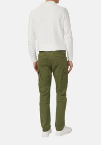 Olivgrüne Cargo-Hose mit schmaler Passform, ausgestattet mit mehreren Seitentaschen, einer glatten Textur und dekorativen Nähten. Kombiniert mit einem weißen Langarmshirt.