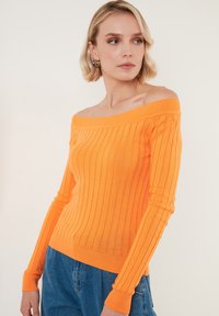Pulover portocaliu cu umerii descoperiți, cu dungi, cu mâneci lungi și design ajustat, realizat dintr-un material tricotat moale.