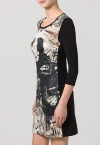 Robe noire à manches trois-quarts ; l'avant présente une impression photographique avec des horloges et le profil d'une femme. Tissu lisse, coupe ajustée.