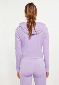 Felpa cropped a maniche lunghe colore lavanda con cappuccio, design senza cuciture e silhouette aderente, abbinata a leggings coordinati. Texture liscia.