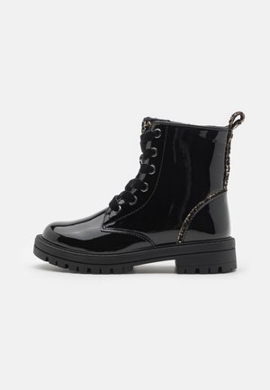 Bottine noire brillante en cuir verni à lacets, avec semelle en caoutchouc épaisse et languette pailletée au talon.