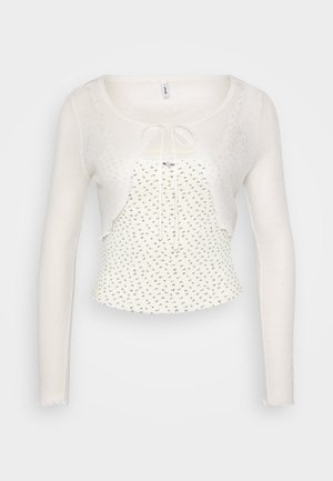 White, sheer cardigan with long sleeves and a tie front. Features a lightweight, textured knit and a fitted, floral-patterned tank underneath.