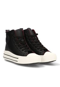 Zapatillas altas negras con suelas de goma blanca y punteras blancas, cordones negros y sutiles detalles de costura roja sobre un fondo blanco.