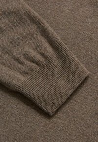 Polsino di un maglione lavorato a maglia marrone che mostra una trama a coste con una finitura liscia. Aspetto leggermente melangiato con sottili variazioni di colore.