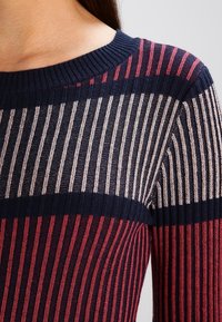 Jersey de punto con rayas verticales en azul marino, rosa y crema. Textura acanalada y diseño de cuello redondo, resaltando el contraste de colores y el patrón.