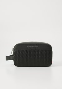 Black toiletry bag with a textured bottom and smooth top, features a zipper, and a side handle. Logo centered on the front.