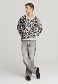 Maglione lavorato a maglia con stampa leopardata nera su sfondo crema, abbinato a jeans a gamba larga grigio chiaro e scarpe nere.
