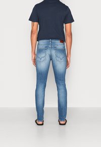 Light blue denim jeans with a slim fit, featuring back pockets and a brown leather patch at the waistband. Worn with a navy T-shirt.