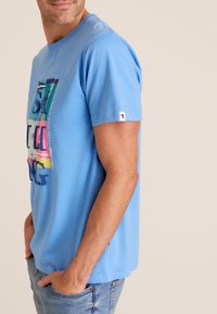 Lichtblauw katoenen T-shirt met korte mouwen, voorzien van een kleurrijke grafische print op de voorkant en een klein logotag op de linker mouw.