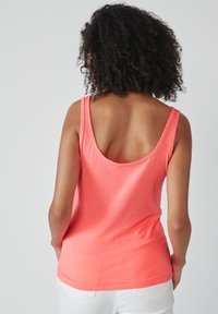 Débardeur corail avec dos nageur et larges bretelles, en tissu doux. Le design est ajusté, mettant en valeur le dos avec une texture lisse.