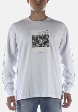 Uomo con camicia bianca a maniche lunghe con foto in bianco e nero della videosorveglianza del negozio e testo che dice "Oops! Ho fatto cadere 1 completo che ho appena rubato."