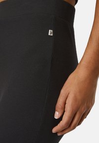 Black ribbed leggings with a high waistband. Features a small logo tag on the side. Smooth texture and form-fitting design.