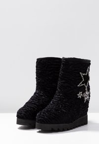 Botas de tobillo de cuña negras con textura, adornadas con estrellas de cristal decorativas en el lado exterior y suelas de goma estriadas.