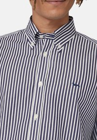 Camicia a righe blu navy e bianche con colletto, dotata di bottoni bianchi e di un piccolo logo ricamato blu sul lato sinistro.