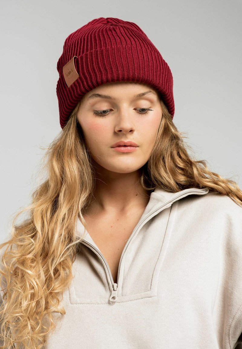 Bordowy dzianinowy beret z prążkowaną teksturą i małą skórzaną naszywką. Noszony z jasnym sweterkiem na zamek.