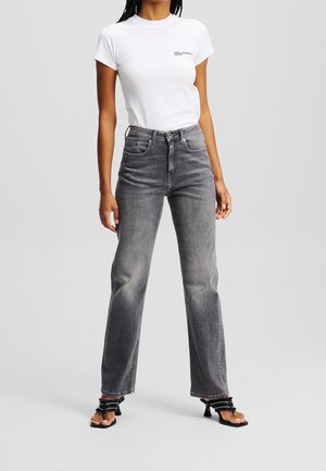 Kvinde iført en hvid t-shirt med logo, højttaljede, falmede sorte jeans med lige ben og sorte åben-toe hælede sandaler.