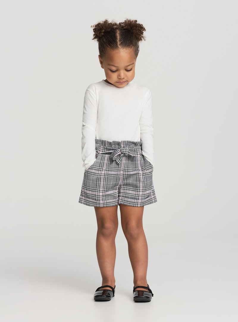 Biała koszula z długim rękawem zestawiona z szarymi szortami w kratę z wiązanym paskiem. Szorty mają kieszenie i teksturowany wzór.