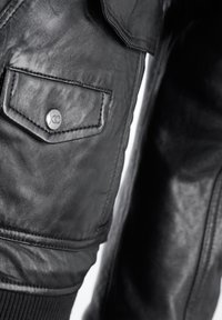 Zwarte leren jas met een patch pocket met een metalen drukknoopsluiting, textuurafwerking, geribde manchetten en gedetailleerde stiksels.