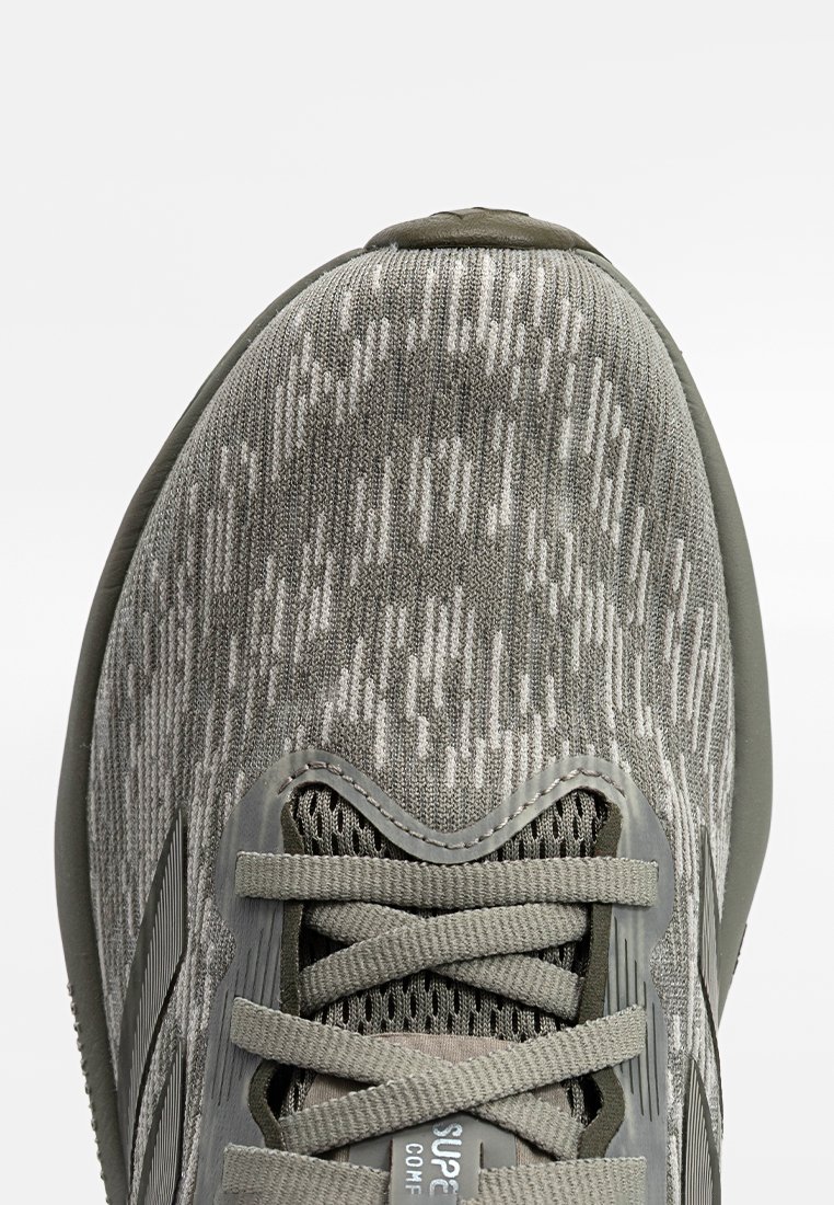 Zapatilla deportiva gris con un upper de punto texturizado que presenta un patrón de luces y sombras, cierre con cordones y una suela acolchada.