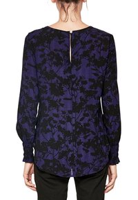 Blusa a maniche lunghe di colore viola con motivo floreale nero, caratterizzata da una chiusura posteriore con bottoni e polsini a sbuffo. Realizzata in tessuto liscio.