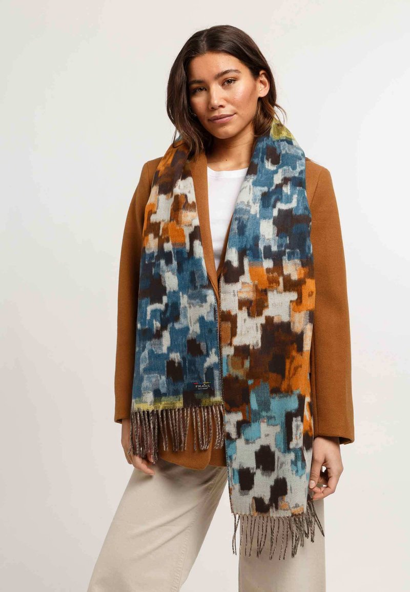 Écharpe colorée à motifs arborant des nuances de bleu, d'orange et de marron, avec des détails de frange. Le tissu semble doux et texturé.