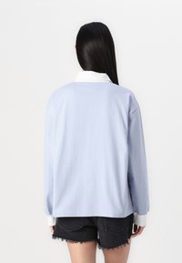 Camicia in cotone azzurro chiaro a maniche lunghe con colletto bianco e polsini a coste, caratterizzata da una vestibilità comoda e un design semplice. Visualizzazione dal retro.